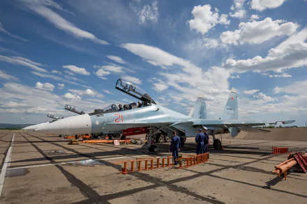 HD desktop wallpaper featuring the military aircraft Sukhoi Su-30. The plane is stationed on a tarmac under a partly cloudy sky, with maintenance crew members visible around it.
