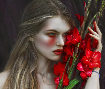 HD PC desktop wallpaper: moody portrait of a woman with pale skin and red cheek makeup, clutching vivid red gladiolus flowers against a dark background.