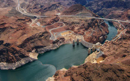 Aerial view of a man-made dam surrounded by rugged landscapes, with a winding river reflecting the sky. This vibrant 4K Ultra HD image showcases the beauty of engineering in nature.