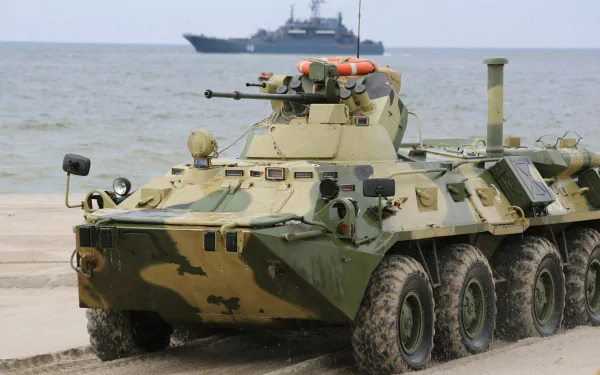 HD military desktop wallpaper featuring a camouflaged BTR-80 armored personnel carrier on a sandy shore with a naval ship in the background.