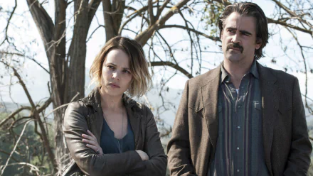 HD desktop wallpaper: two actors as detectives in the TV show True Detective — a woman with arms folded and a mustached man standing in front of bare trees.