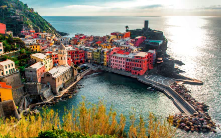 Colorful houses of the Vernazza village along the rugged Cinque Terre coastline in Italy, overlooking the calm sea under a bright sky.