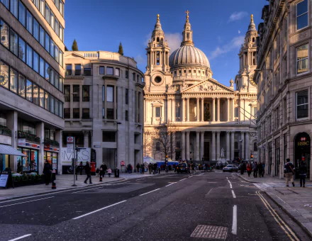 HD image of a bustling London street leading to a grand cathedral. The detailed architecture of the church stands out against the clear sky, framed by buildings on either side.