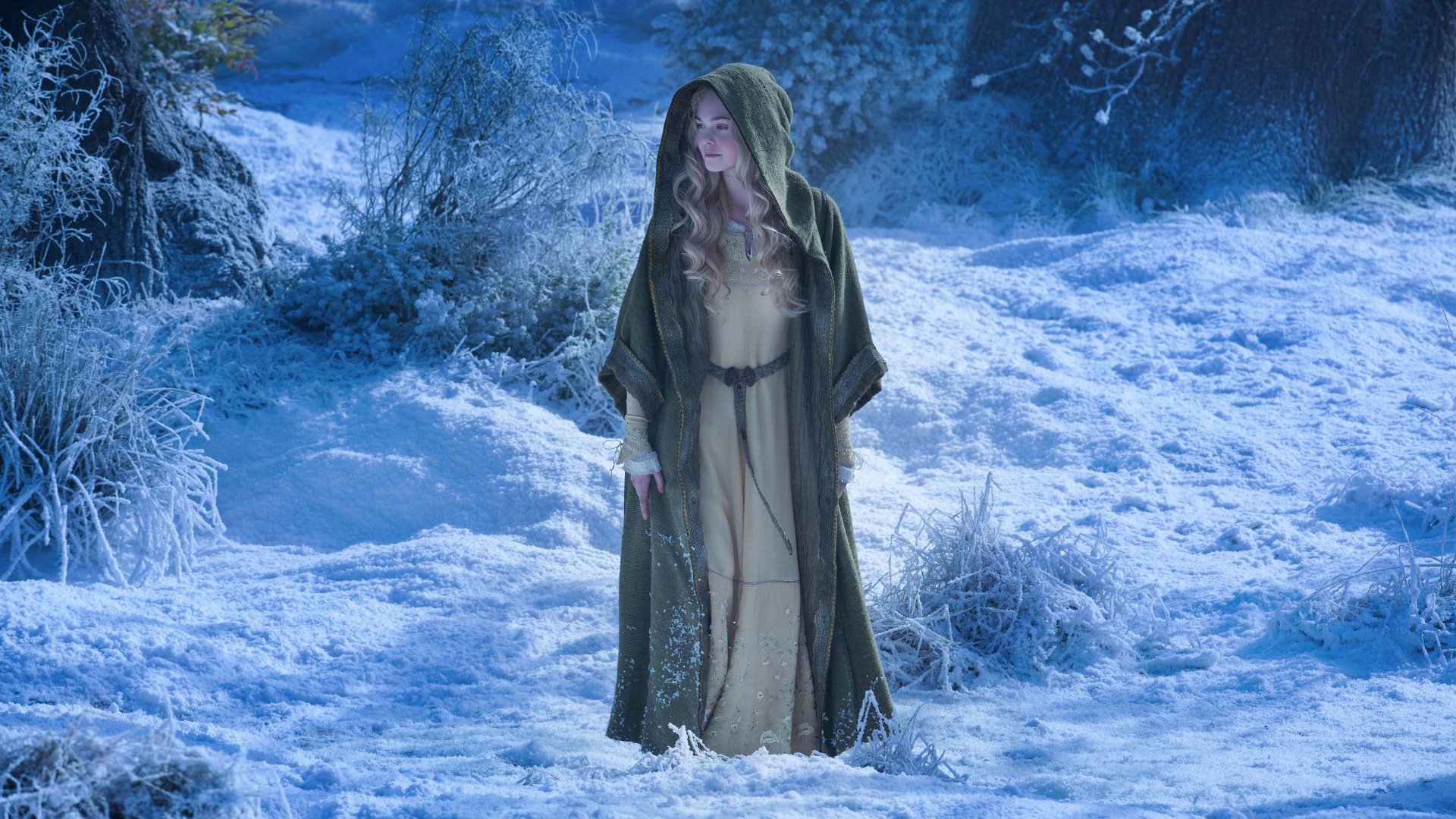 HD PC desktop wallpaper featuring a scene from the movie Maleficent with a woman in a hooded cloak standing in a snowy, mystical forest.