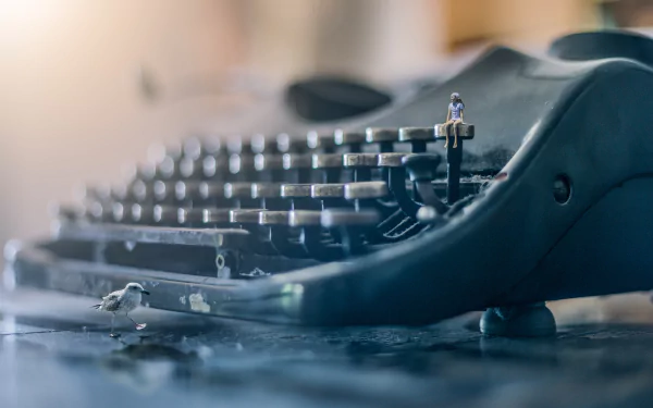Close-up 4K Ultra HD wallpaper of a vintage typewriter with a tiny man figure sitting on a key, set against a blurred bokeh background.