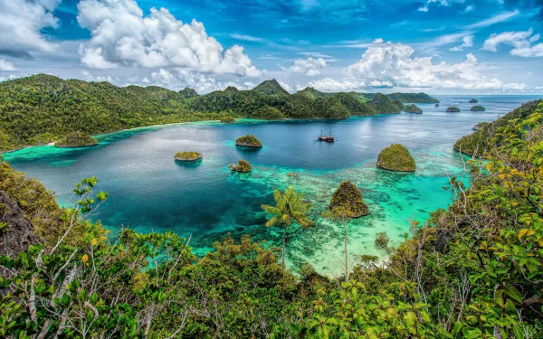 A vibrant HD desktop wallpaper of Ha Long Bay, Vietnam, featuring turquoise waters, lush palm trees, rocky islands, and boats under a bright blue sky.