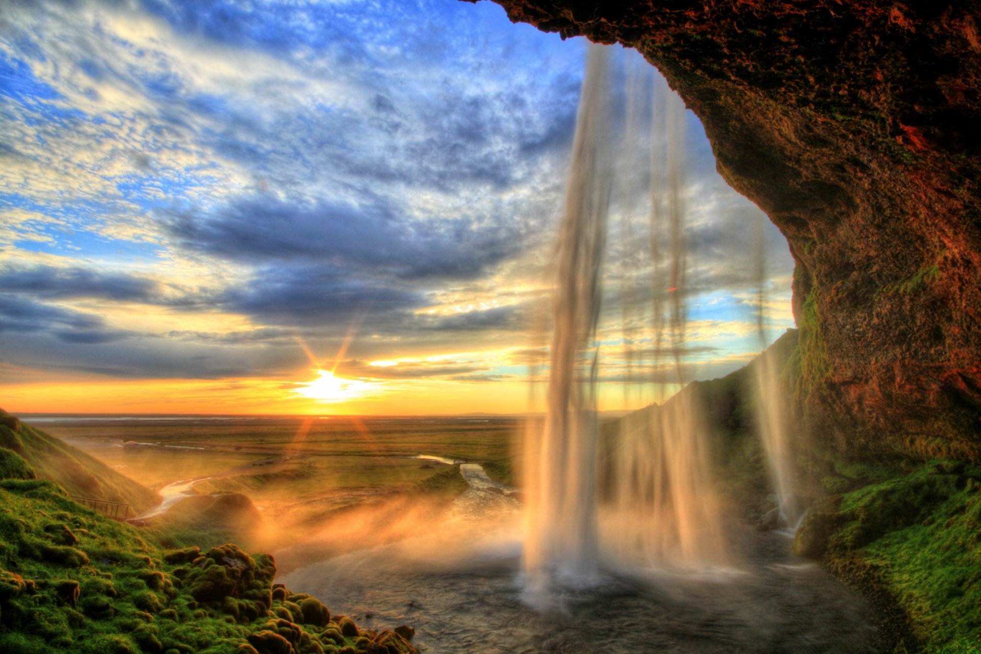 Seljalandsfoss waterfall in Iceland at sunset, viewed from behind the falls with a mossy cave framing the misty coastline — 2K Quad HD PC wallpaper.