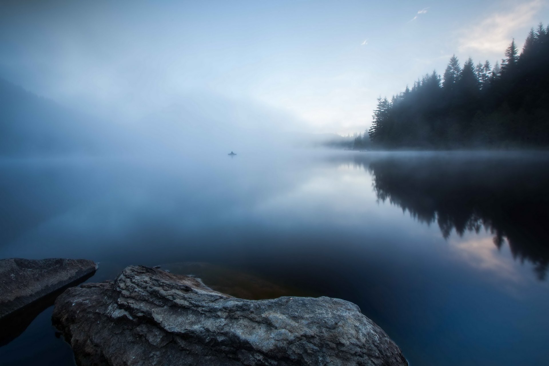 HD desktop wallpaper of a serene foggy lake with still water reflecting mist-covered trees and a rocky shore, capturing peaceful nature and quiet reflection.