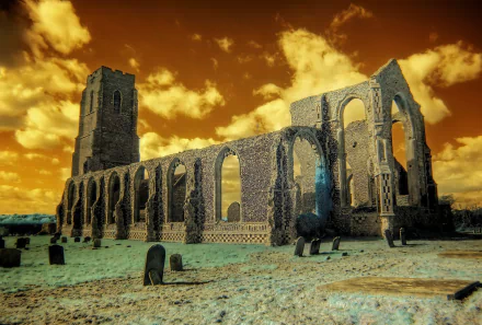 Infrared photography of a ruined stone abbey and gravestones under a fiery orange sky — 2K Quad HD PC desktop wallpaper and background.