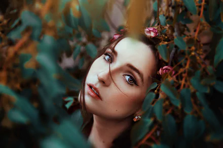HD desktop wallpaper featuring a brunette woman with brown eyes, wearing lipstick and floral earrings, framed by foliage with a soft bokeh background.