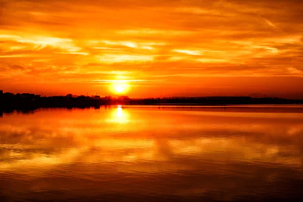 HD PC desktop wallpaper photograph: orange sunset with the sun over a calm lake, sky and sun reflected on the water across a serene landscape.