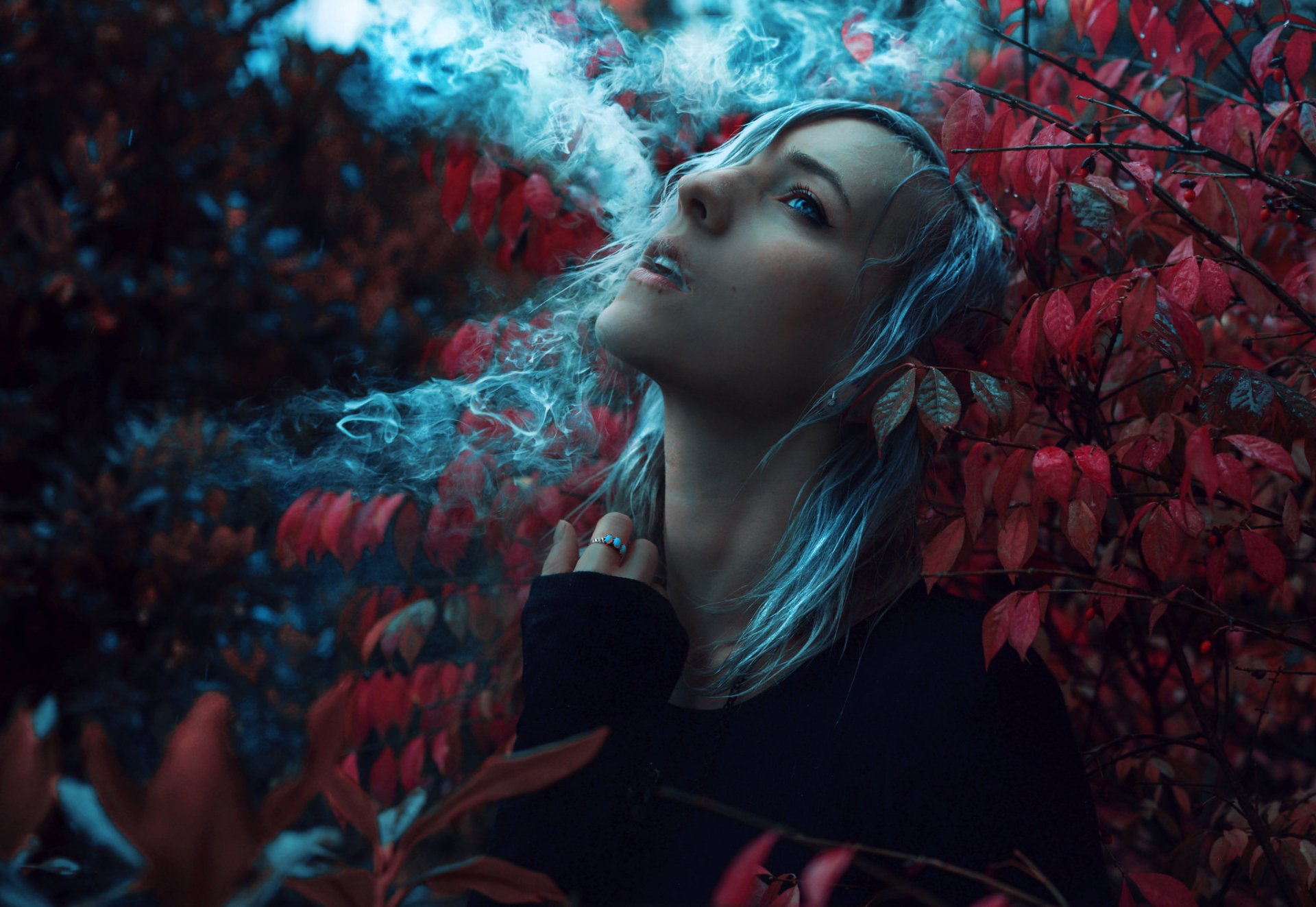 A model with white hair exudes a moody vibe, surrounded by vibrant red foliage and wisps of smoke, creating a stunning bokeh effect in this HD desktop wallpaper.