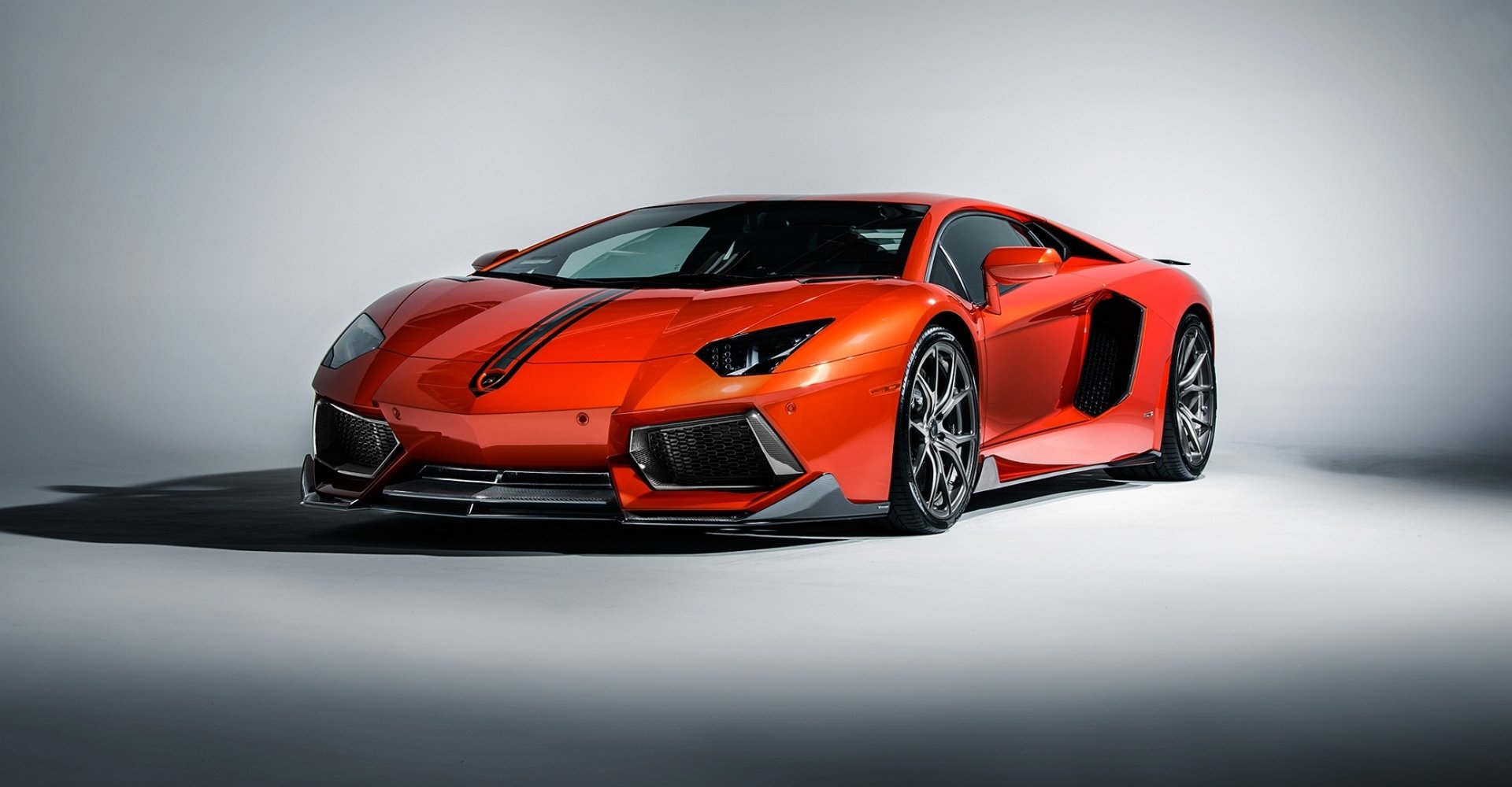 HD desktop wallpaper featuring an orange Lamborghini Aventador LP 700-4 supercar parked in a studio setting, highlighting its sleek design and aggressive stance.