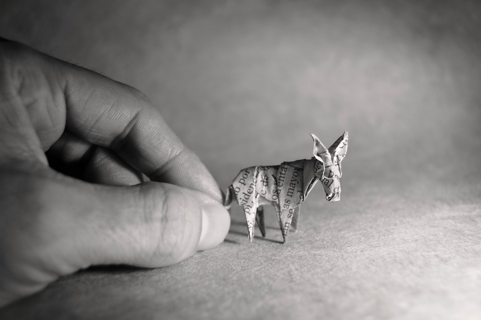 Black and white close-up of a hand holding a small origami donkey, captured as a high-definition PC desktop wallpaper and background.