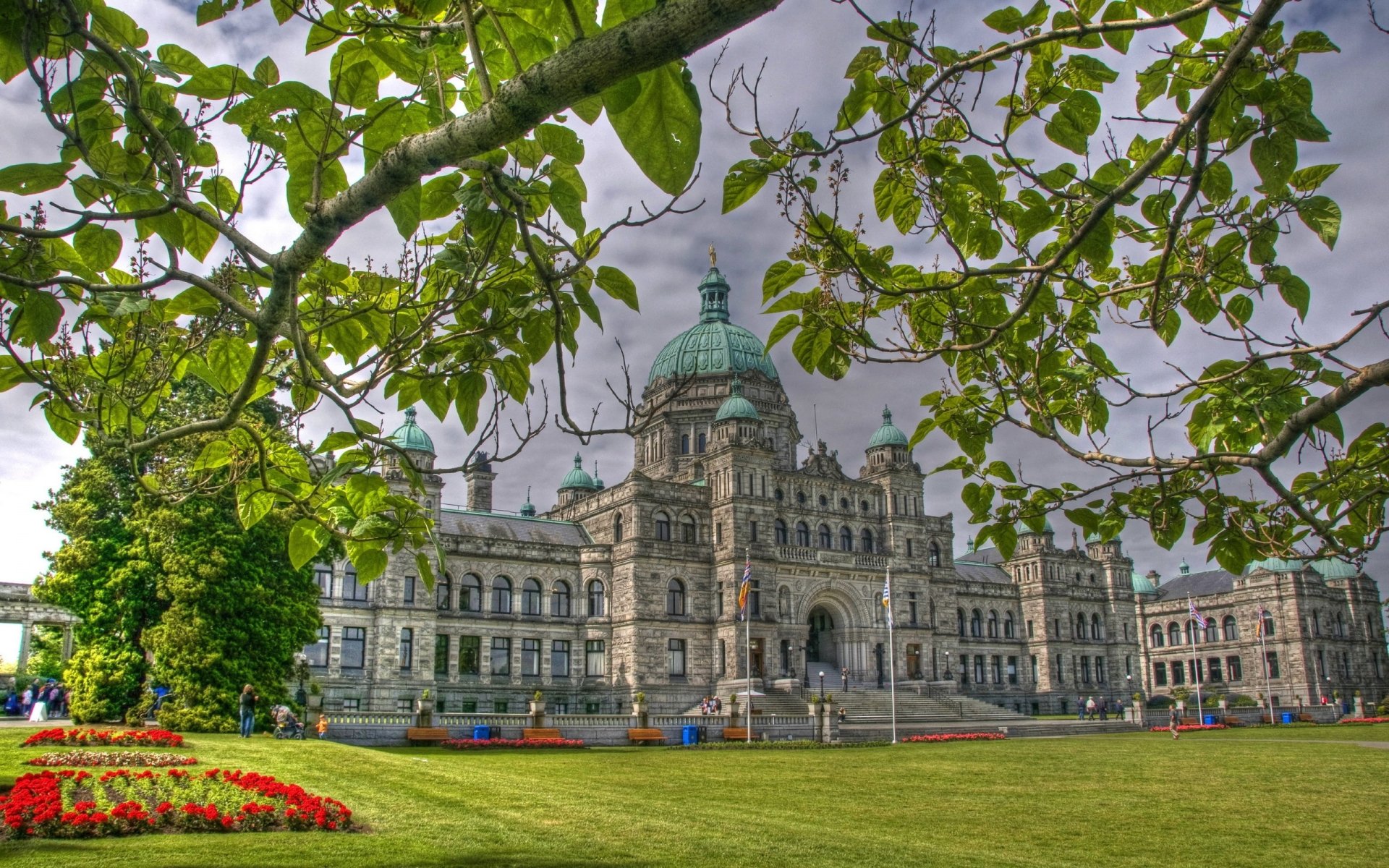 View of the Parliament of Canada on Parliament Hill, featuring its iconic dome and detailed architecture framed by green foliage and a manicured lawn.