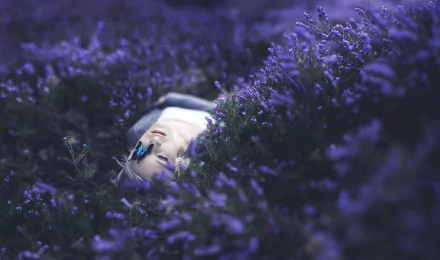 A blonde woman lies peacefully among purple flowers with a butterfly resting on her face, surrounded by a soft bokeh effect in this HD desktop wallpaper.
