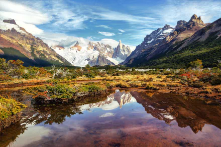A stunning landscape of the Andes in Patagonia, Argentina, featuring a reflective lake surrounded by majestic mountains and lush greenery under a vibrant sky.