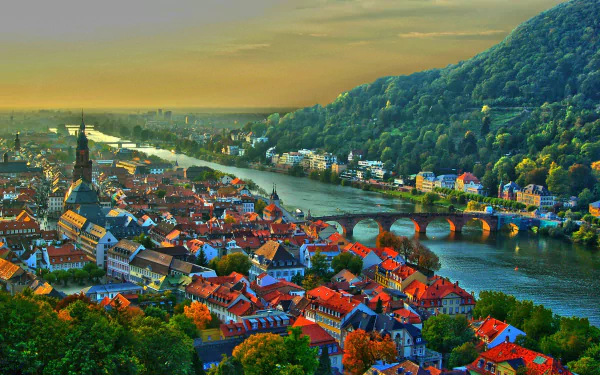 A vibrant cityscape of Heidelberg, Germany, featuring historic buildings, a stone bridge over the river, and lush green hills under a golden sunset sky.