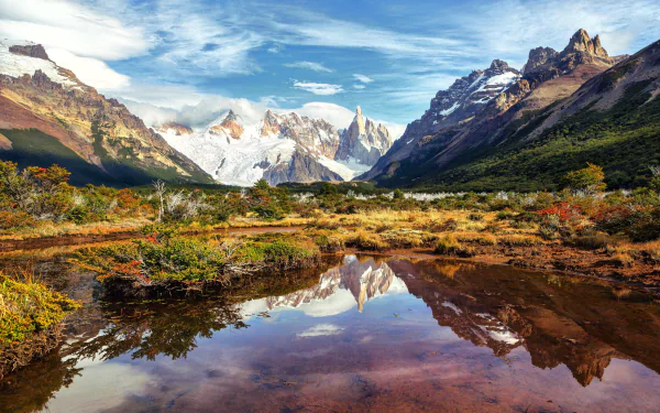 A stunning landscape of the Andes in Patagonia, Argentina, featuring a reflective lake surrounded by majestic mountains and lush greenery under a vibrant sky.