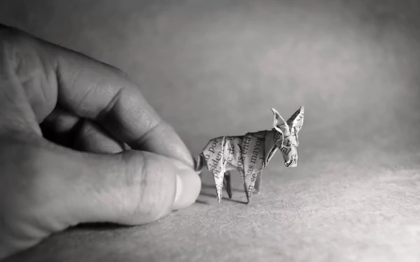 Black and white close-up of a hand holding a small origami donkey, captured as a high-definition PC desktop wallpaper and background.