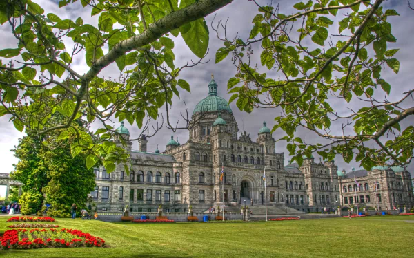 View of the Parliament of Canada on Parliament Hill, featuring its iconic dome and detailed architecture framed by green foliage and a manicured lawn.