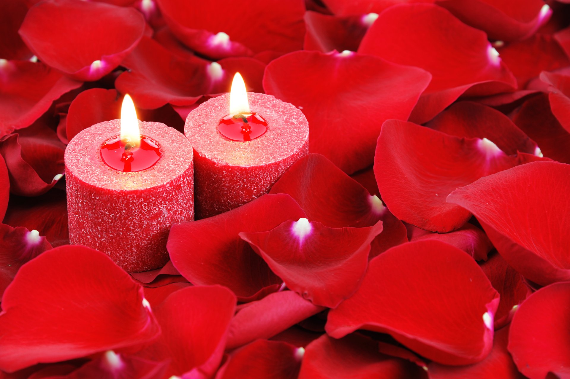 A 4K Ultra HD desktop wallpaper featuring two glowing red candles surrounded by vibrant red petals in a close-up photography composition.