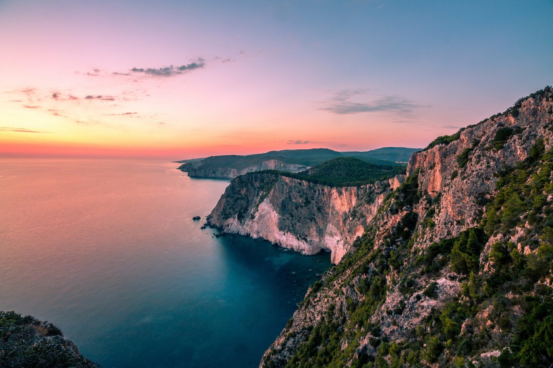 HD desktop wallpaper showcasing the stunning coastline of Zakynthos, Greece, with rugged cliffs overlooking a calm ocean at sunset on the horizon.