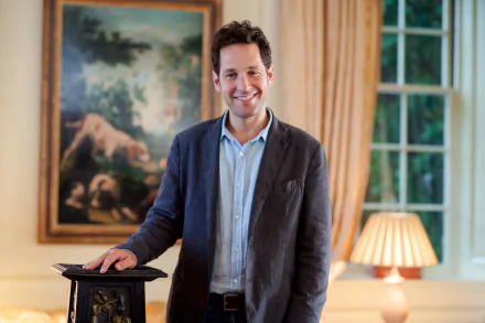 HD desktop wallpaper featuring American actor and celebrity Paul Rudd standing indoors, smiling, with a framed painting and lamp in the background.