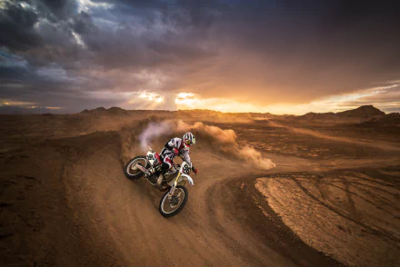A motocross rider races on a dirt track through rugged landscape under a dramatic sunset sky, captured in high-definition for a dynamic sports wallpaper.