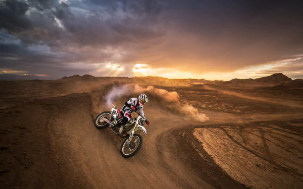 A motocross rider races on a dirt track through rugged landscape under a dramatic sunset sky, captured in high-definition for a dynamic sports wallpaper.