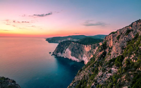 HD desktop wallpaper showcasing the stunning coastline of Zakynthos, Greece, with rugged cliffs overlooking a calm ocean at sunset on the horizon.