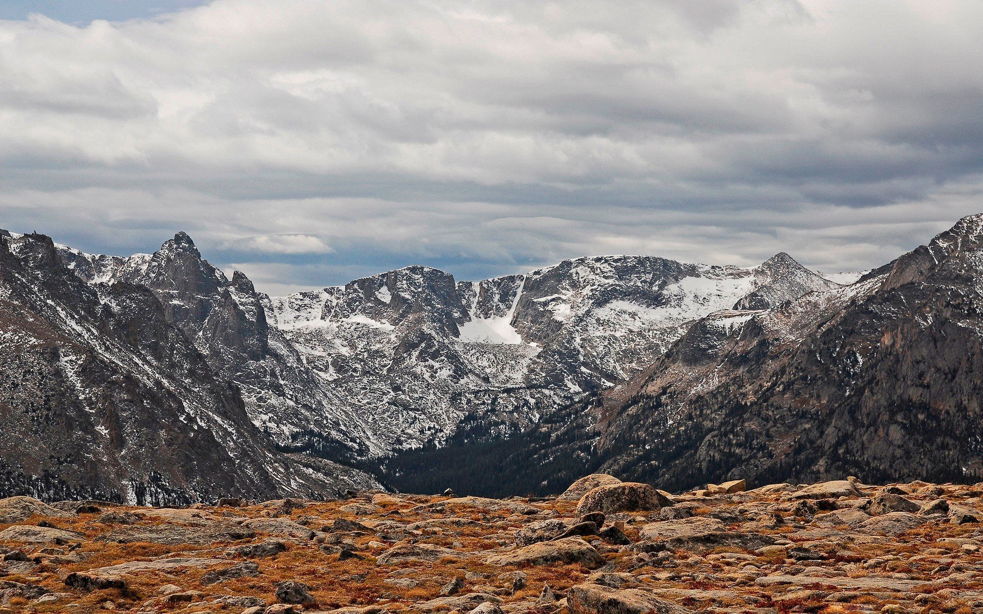 HD PC desktop wallpaper showcasing a dramatic mountain landscape under a cloudy sky with rocky terrain in the foreground.