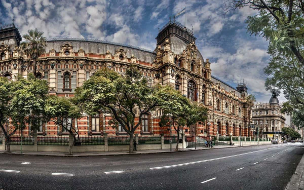 A vibrant street in Buenos Aires showcases stunning architecture, with lush trees framing a historic building under a dramatic sky. HDR photography captures the city's beauty.