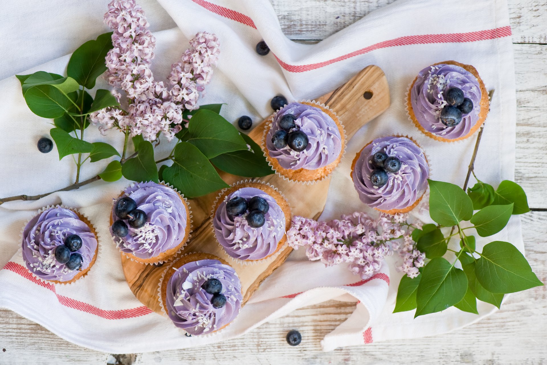 A 4K Ultra HD desktop wallpaper featuring lilac-colored blueberry cupcakes arranged on a wooden board with fresh green leaves and lilac flowers.