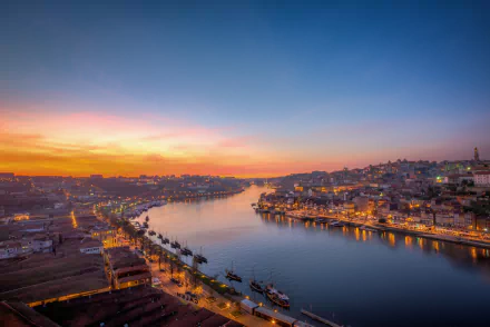 Evening cityscape of Porto, Portugal, with a calm river reflecting city lights under a colorful dawn sky, captured in HD for a desktop wallpaper background.