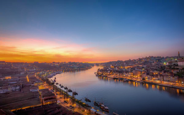 Evening cityscape of Porto, Portugal, with a calm river reflecting city lights under a colorful dawn sky, captured in HD for a desktop wallpaper background.
