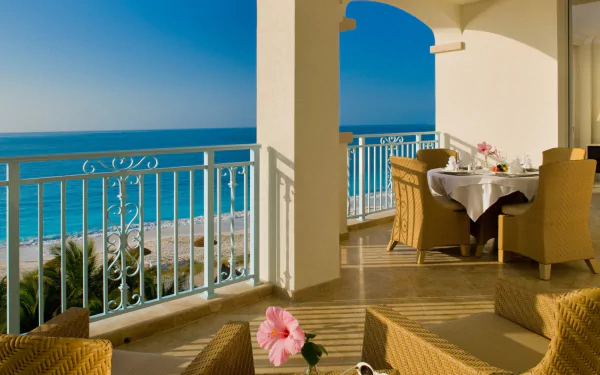 Holiday HD desktop wallpaper: sunlit house terrace with wicker chairs and table topped with hibiscus, man-made railing framing a calm ocean horizon.
