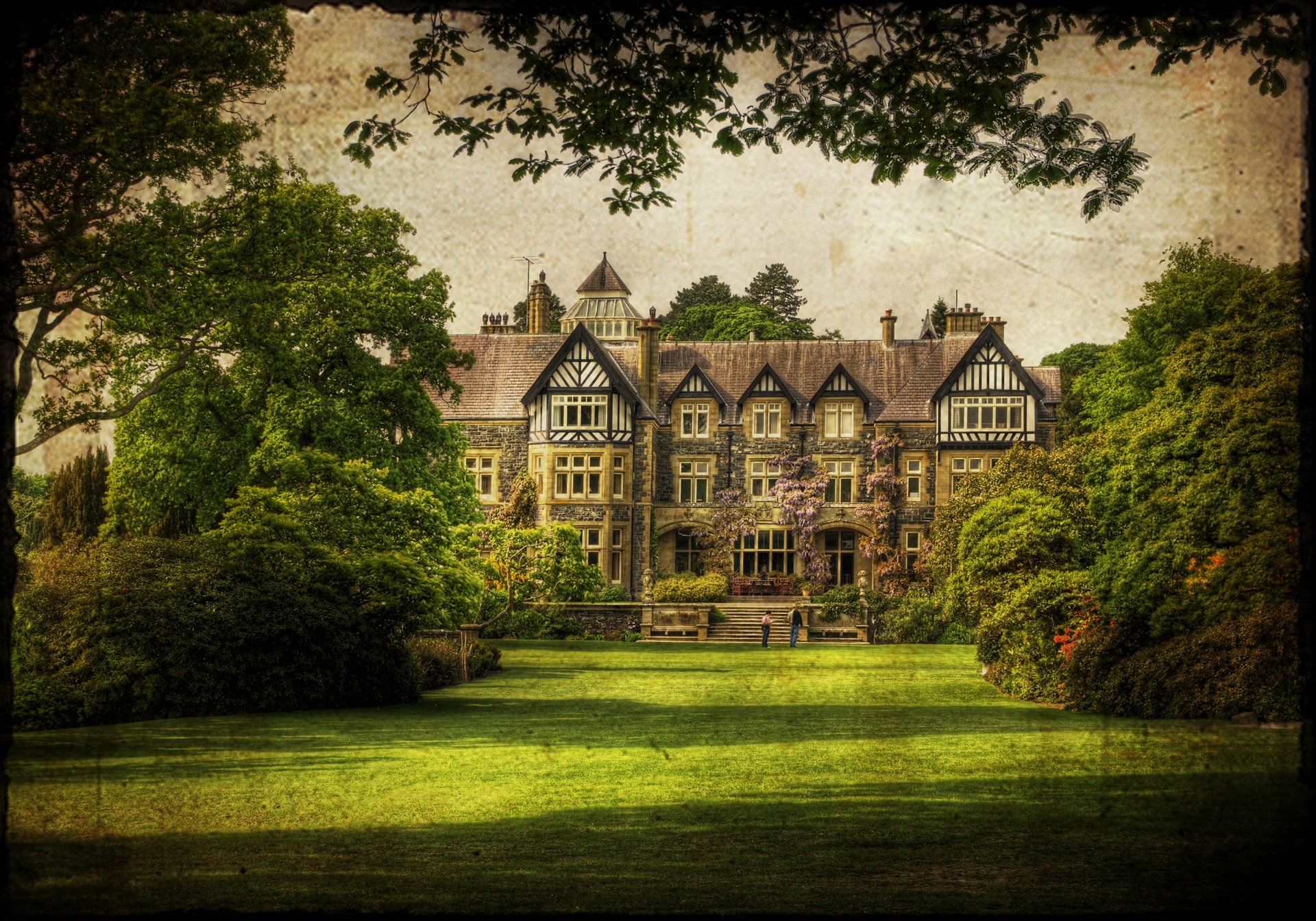 A stunning view of Bodnant Gardens in Wales featuring a grand architectural building surrounded by lush greenery and trees, creating a serene atmosphere great for desktop wallpaper.