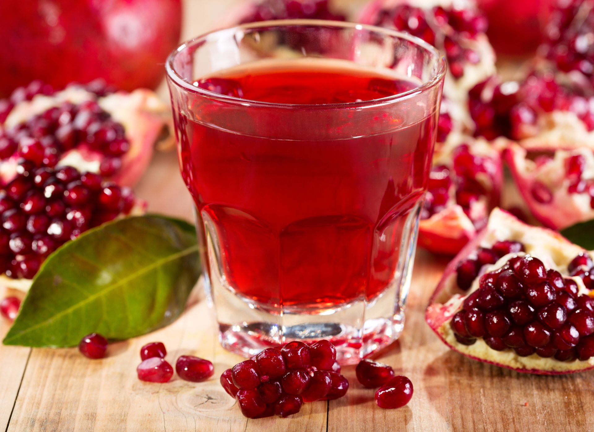 4K Ultra HD PC desktop wallpaper background: glass of ruby pomegranate juice with pomegranate halves and scattered seeds on a wooden board, food photography.