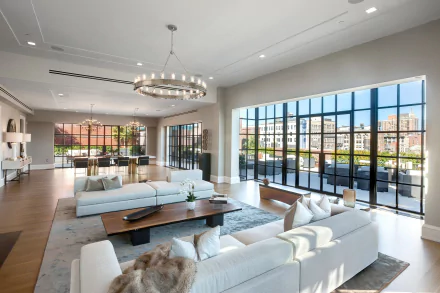 A modern living room featuring a large couch, a coffee table, cushions, and expansive windows offering a view, complemented by elegant decor and ample natural light.