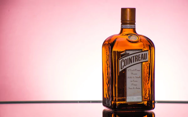 Minimalist HD desktop wallpaper featuring a bottle of Cointreau liquor against a soft pink background, highlighting a stylish blend of drink and food themes.