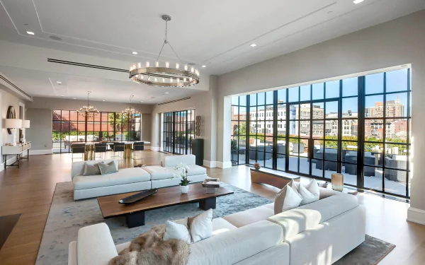 A modern living room featuring a large couch, a coffee table, cushions, and expansive windows offering a view, complemented by elegant decor and ample natural light.