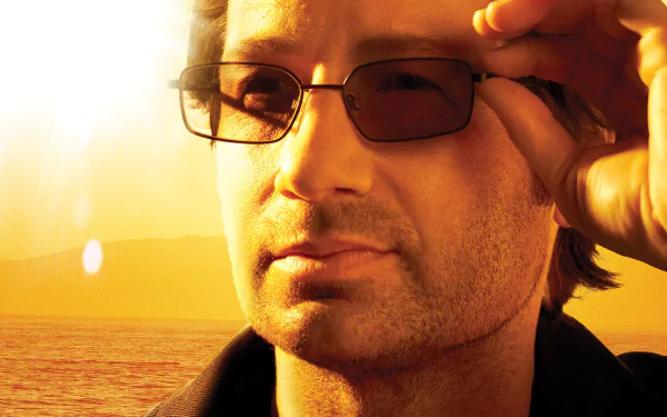 HD PC desktop wallpaper: close-up of Hank Moody (TV show Californication) adjusting sunglasses against a warm golden ocean sunset.
