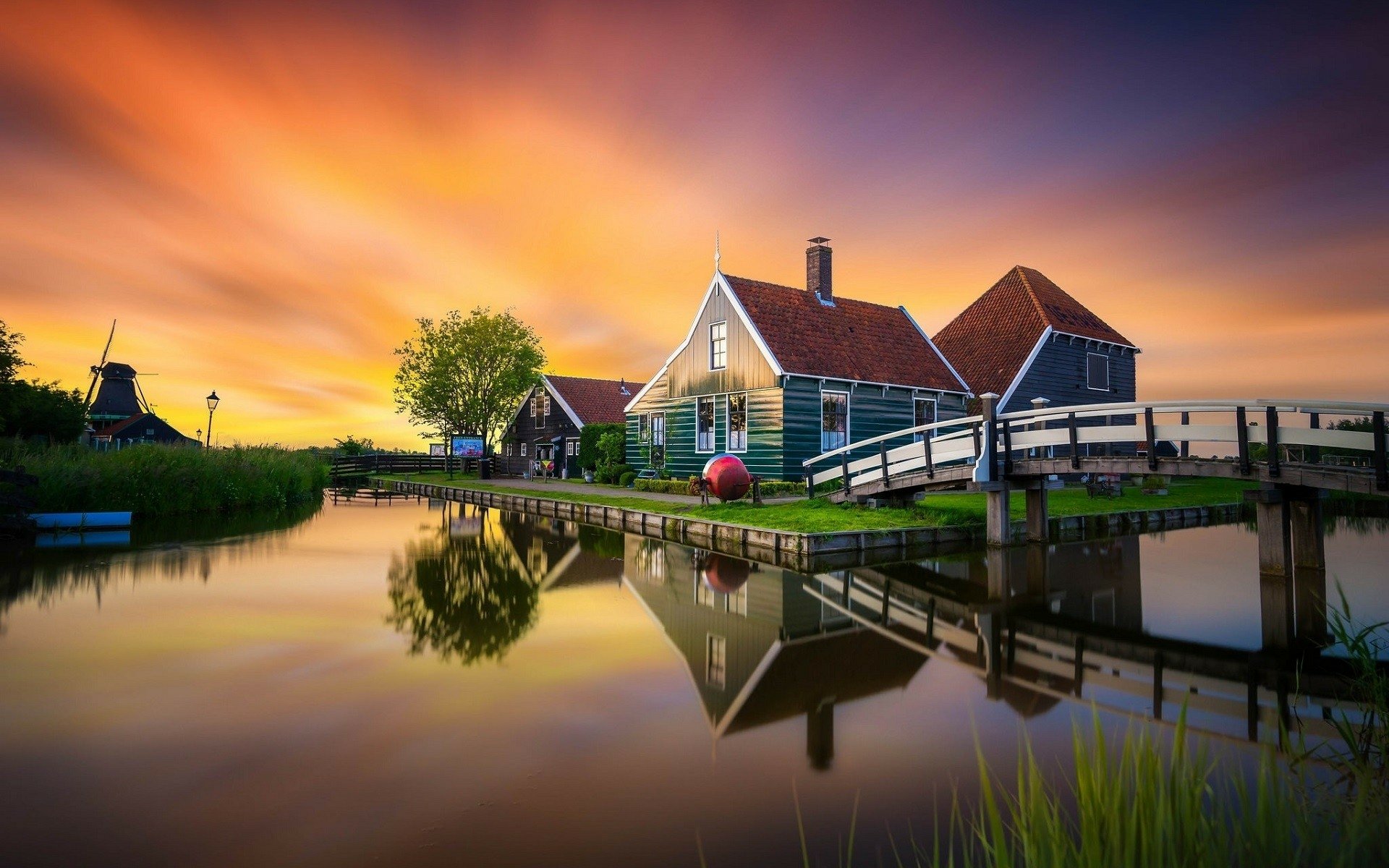 Sunset over a Dutch canal featuring a traditional house, a windmill in the distance, and a bridge, captured in vibrant colors as an HD PC desktop wallpaper.