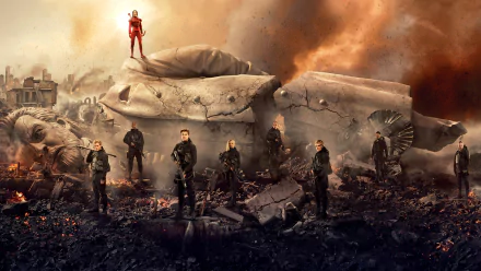 HD PC desktop wallpaper of The Hunger Games: Mockingjay - Part 2 — a group of fighters in dark gear stand amid rubble and a shattered statue, one lone figure in red atop the ruins beneath a smoky sky.