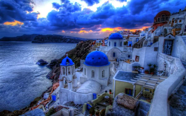 A stunning HDR image of Santorini, Greece, showcasing vibrant clouds and a sunset sky over whitewashed houses with blue domes, set against the glistening sea.