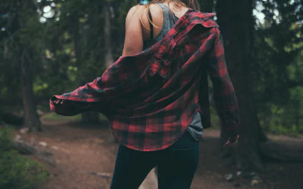 HD desktop wallpaper of a woman model in jeans and a red plaid shirt, shown from the rear, walking through a forested area.