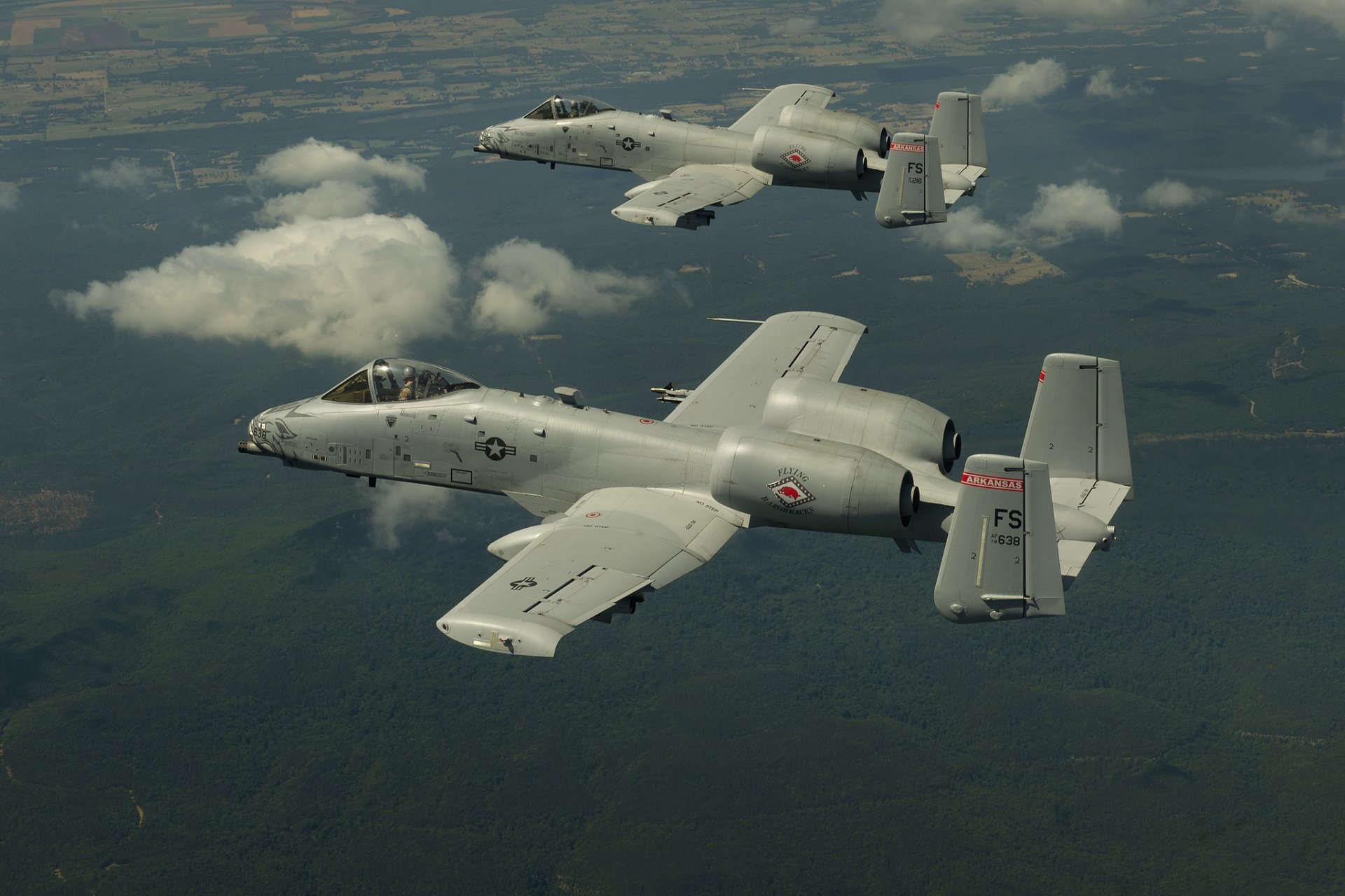 Two Fairchild Republic A-10 Thunderbolt II warplanes fly above clouds and land, captured in an HD desktop wallpaper featuring military jet fighters.