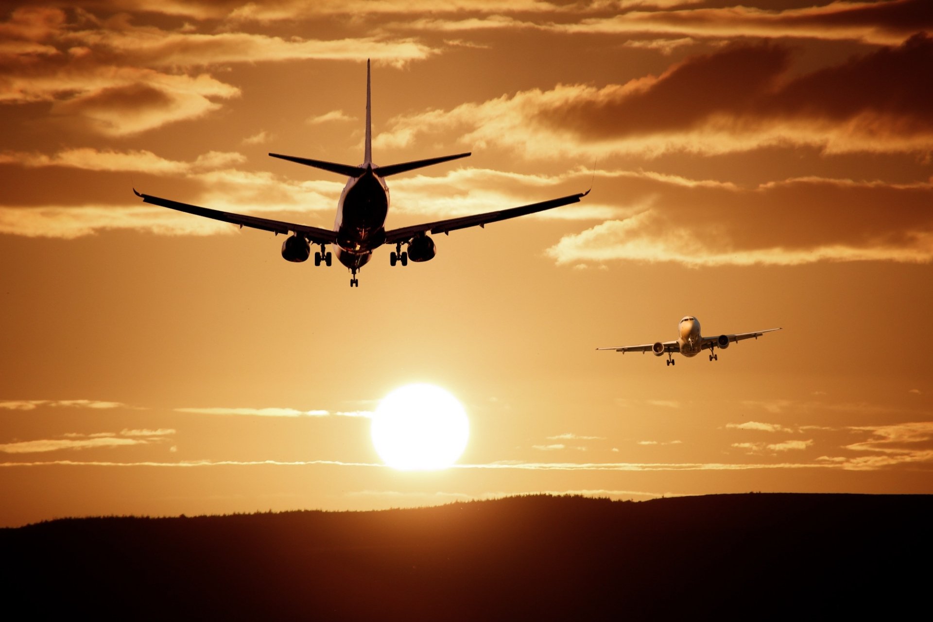 Two passenger airplanes fly against an orange sunset sky with clouds, creating a dramatic HD desktop wallpaper featuring aircraft and a glowing sun.