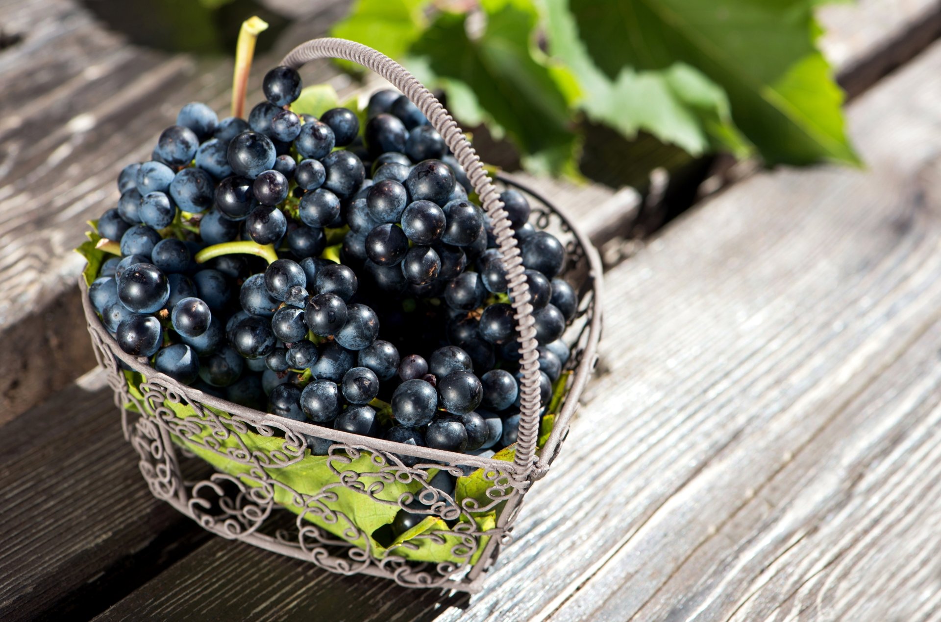 A decorative basket filled with dark grapes resting on a weathered wooden surface, captured in sharp detail as an 8K Ultra HD PC desktop wallpaper.
